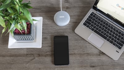 A phone sits next to a Google speaker on a desk