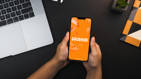 A person holding a phone showing the Grubhub logo