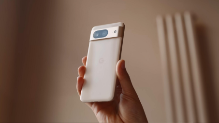 A beige colored Google Pixel 8 held in the air by a hand