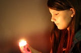 A girl in side profile looking at a candle she is holding.