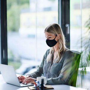 A woman wearing a mask works at a computer in an office