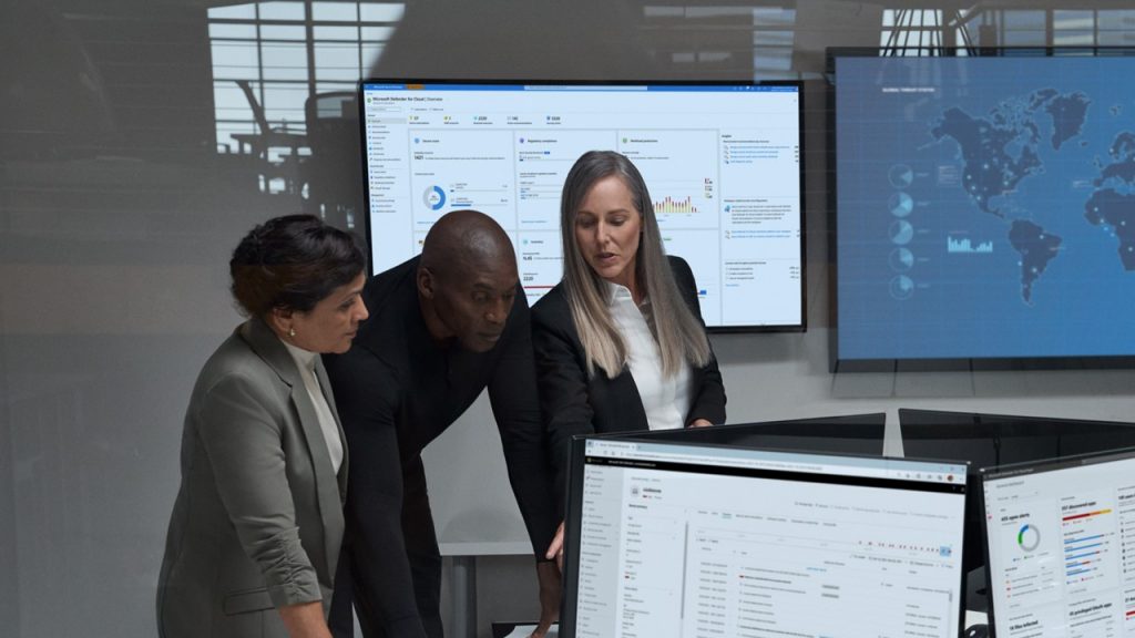 Three people standing in a security operations cetnre with screens representing cyber threat landscape