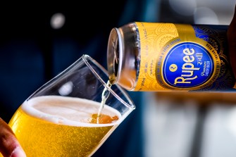 Rupee Beer being poured from a can into a pint glass
