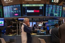 Traders walking on the floor at the New York Stock Exchange in front of a screen displaying the GameStop logo.