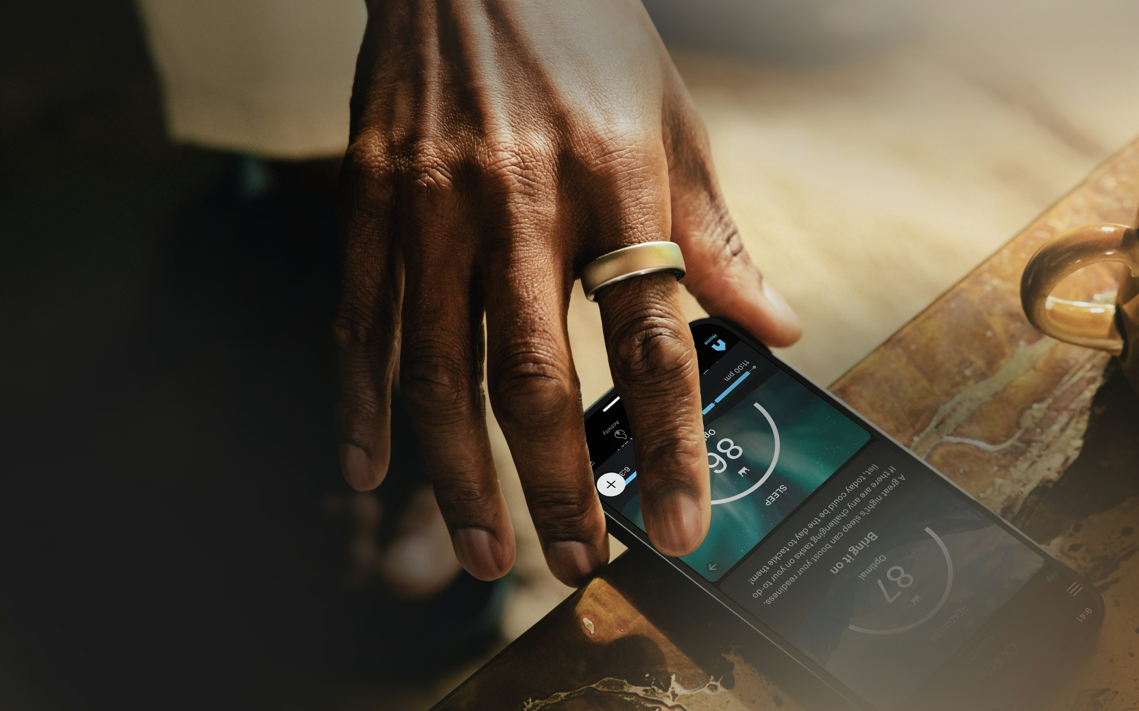 Oura Ring featured on a hand reaching for a mobile device with the Oura app open