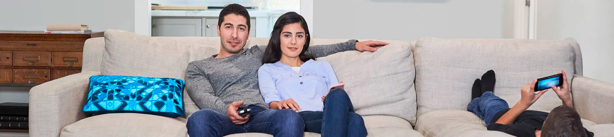 Par använder TV-fjärrkontroll i soffan medan barnet använder smartphone