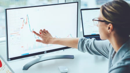 Business woman sitting at desk, pointing to graph on computer screen