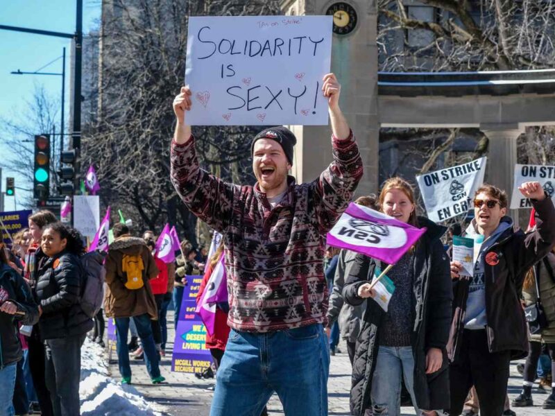 A TA holds up a sign that reads "solidarity is sexy" during a picket.
