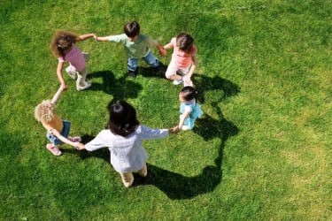 Børn der danser rundt i en cirkel på en grøn plæne