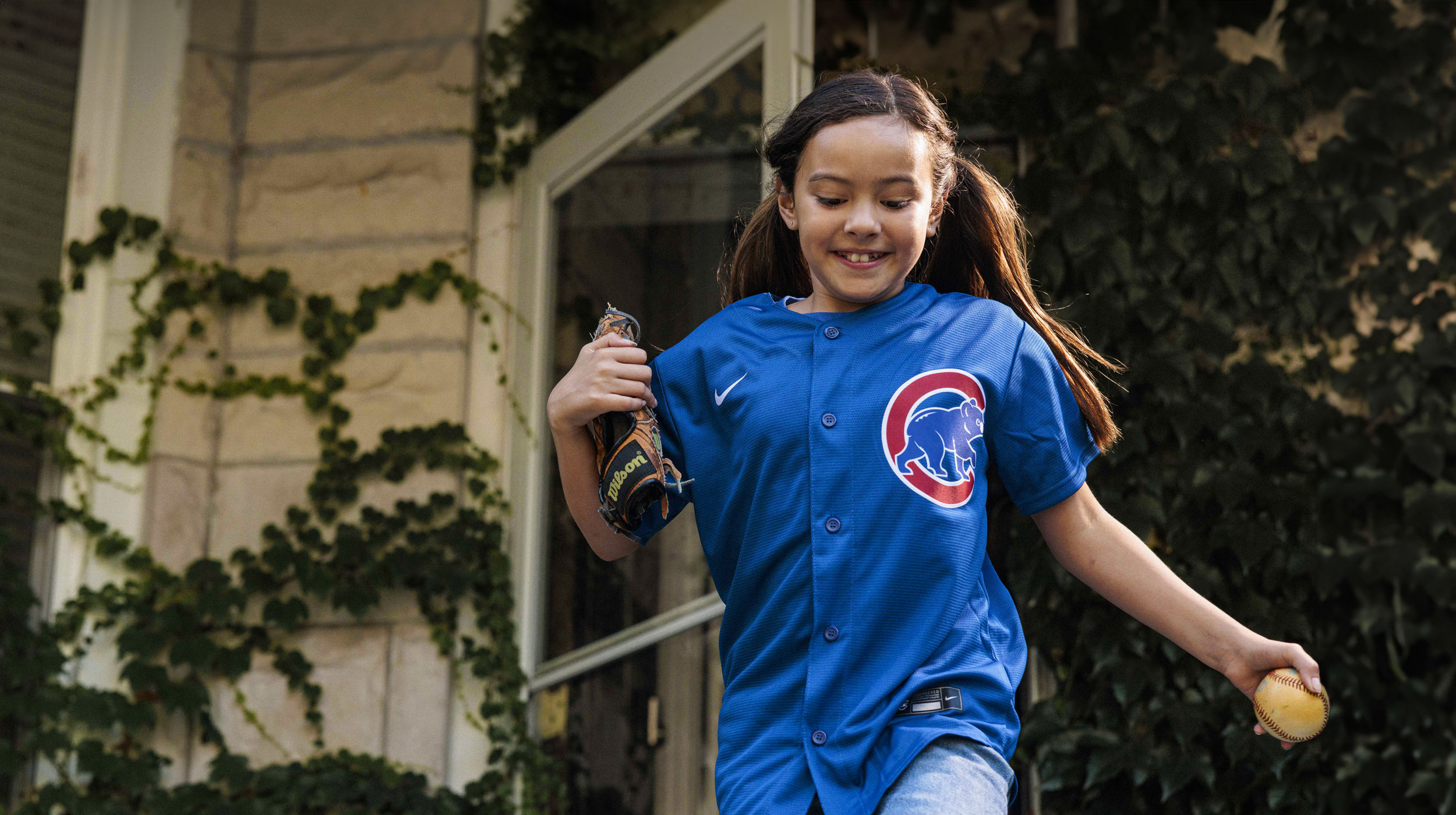 Young girl in Chicago Cubs jersey running and carrying baseball mitt