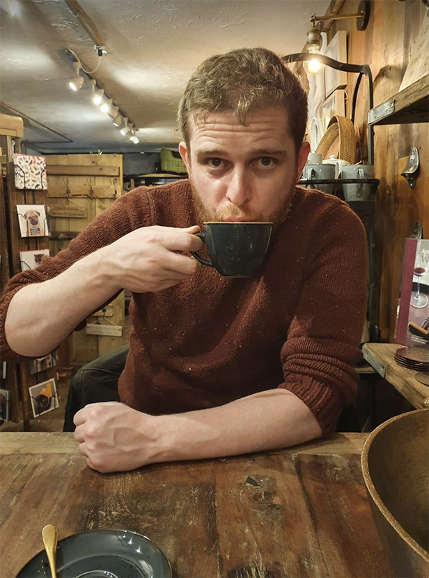 "Chris sitting at a table indoors holding a mug "