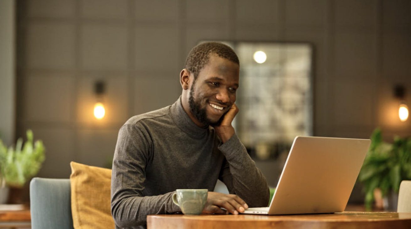 يبدو خريج شهادة Google المهنية، Ousman Jaguraga، سعيدًا أثناء عمله على جهاز الكمبيوتر المحمول الخاص به.