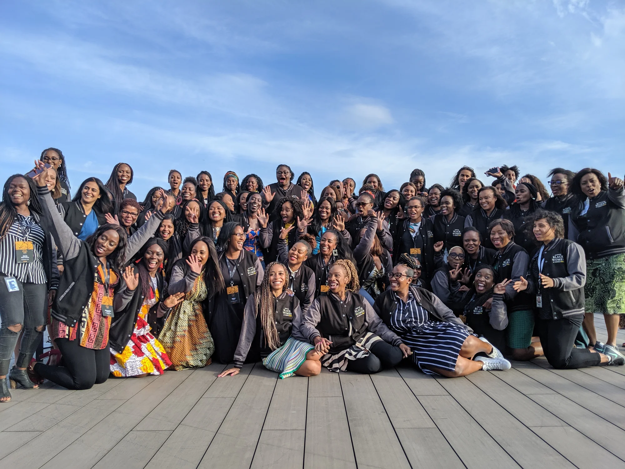 A group of Googlers, all women, bunched together waving, or showing piece signs for a large group photo