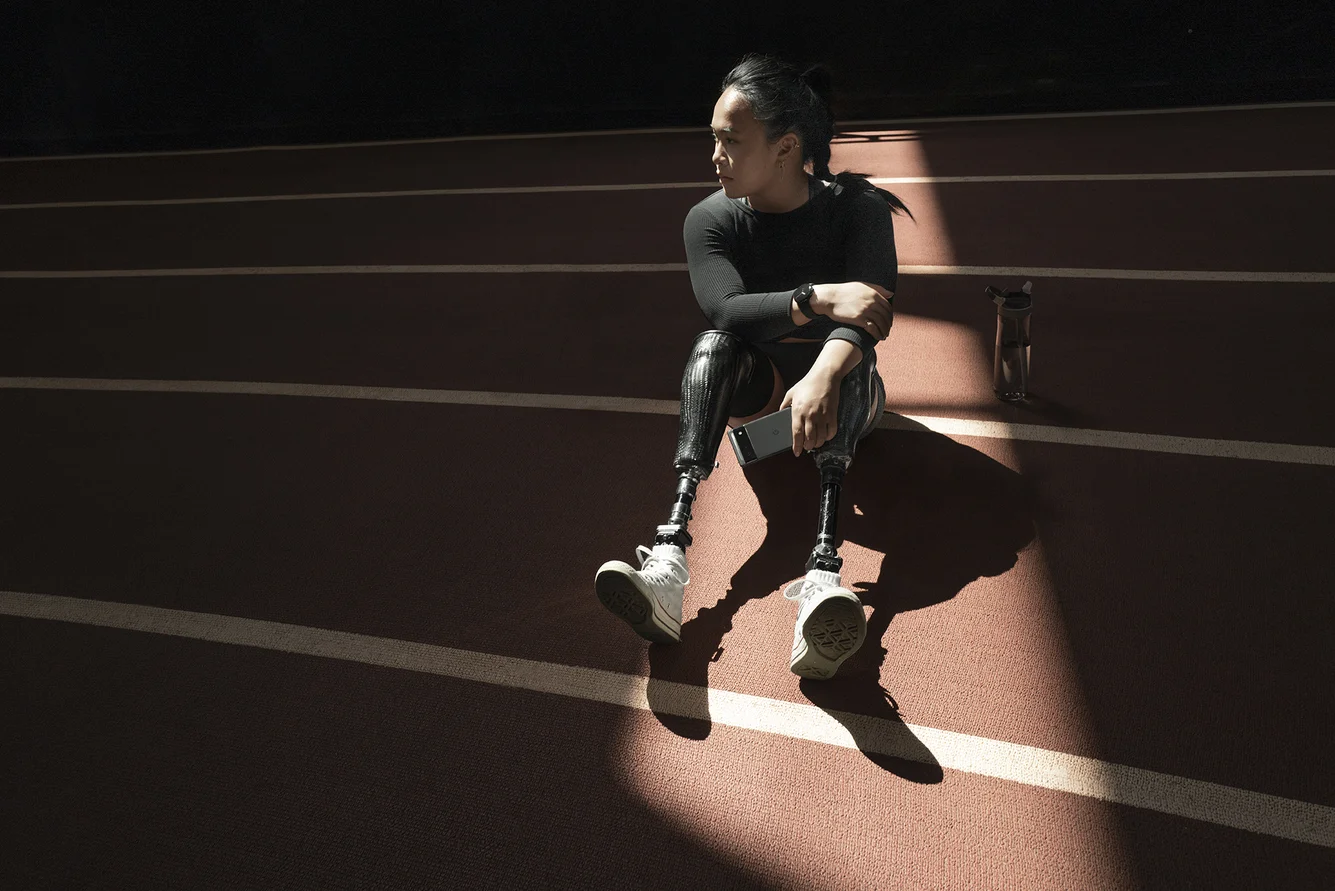 A runner sits on a track in a spot of light wearing a Google Pixel Watch.
