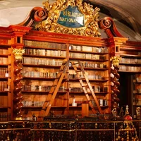 A book section of The National Library hall with intricate woodwork, featuring a grand bookcase filled with old books, a decorative railing, and a wooden ladder for accessing higher shelves.