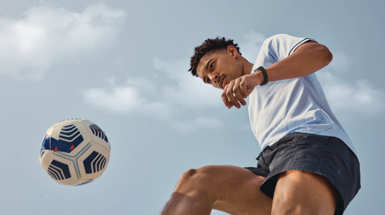 A photograph of a young man wearing athleisure clothing and playing soccer with Inspire 3 on his wrist.
