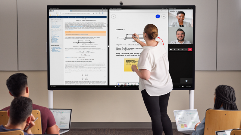 En lærer er foran en klasses og skriver på en Hub 85" med en lysegrå Surface-penn. Edge Whiteboard og Teams er på skjermen. I forgrunnen har flere elever en Pro 7+ og tar notater i One Note.