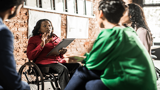 Poslovna žena u invalidskim kolicima vodi grupnu diskusiju u kreativnoj kancelariji
