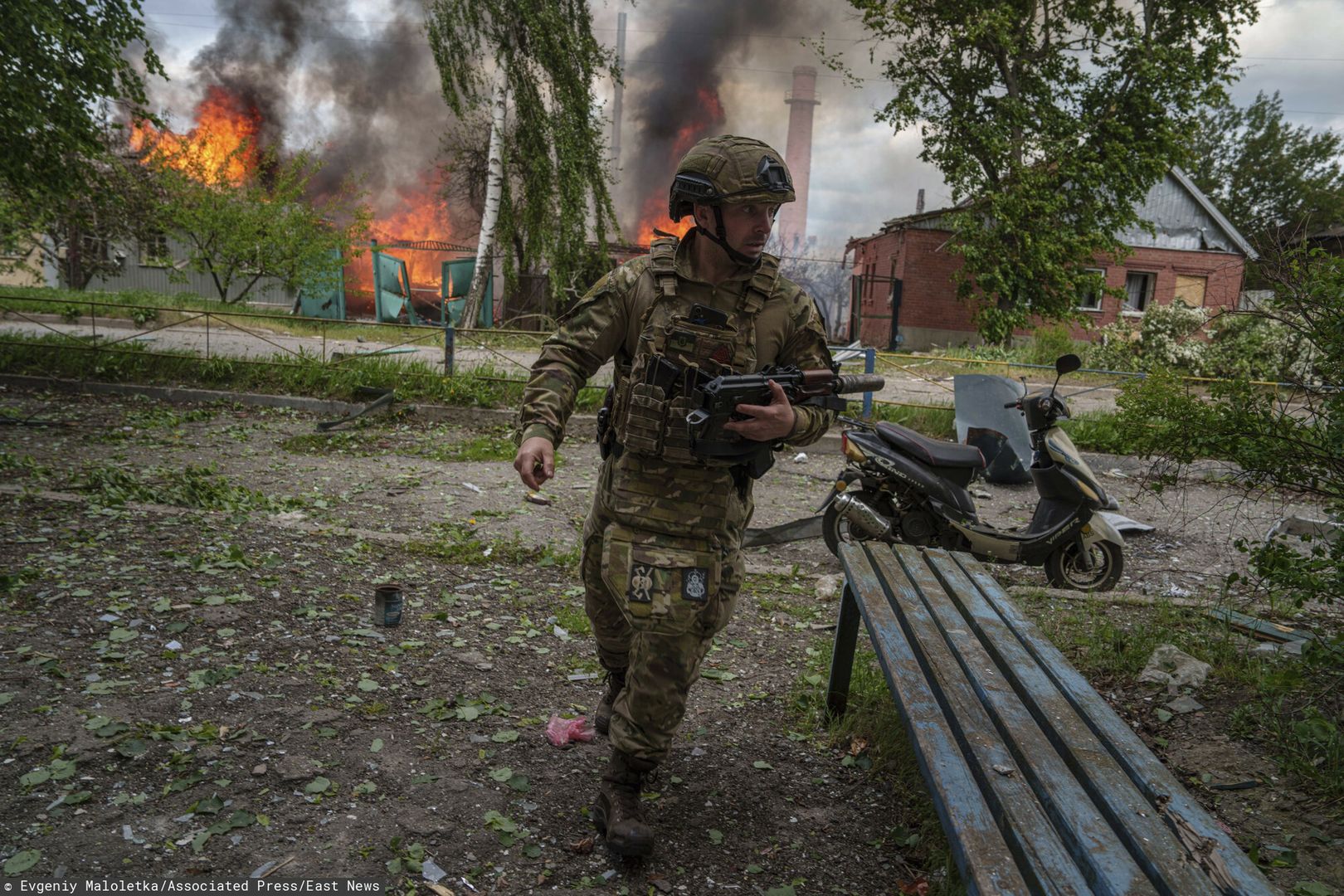 Wołczańsk, 11 maja 2024 r. Ukraiński policjant biegnie na pozycję. W tle budynki płonące po rosyjskim ataku