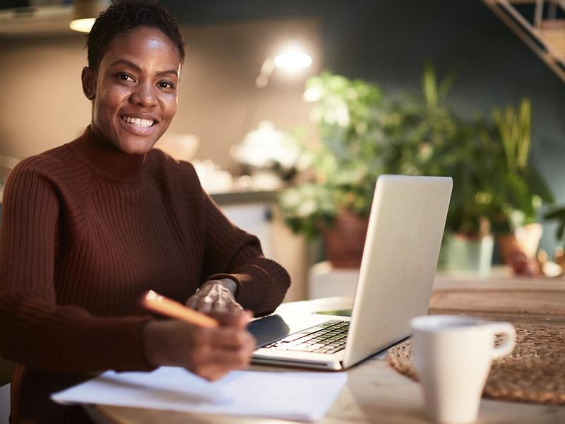 Smiling person holding a pen and working in front of a laptop