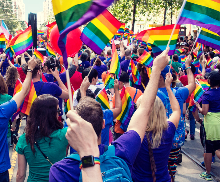Fotografia de uma multidão numa parada a agitar bandeiras arco-íris. 
