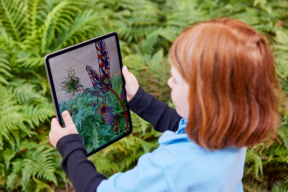 En ung elev holder opp iPad Pro for å utforske plantelivet utendørs gjennom Deep Field-appen.
