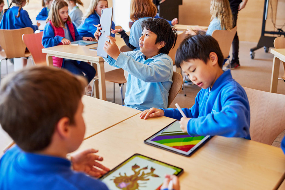 Jovens estudantes reunidos em uma mesa usam o iPad Pro e o Apple Pencil.