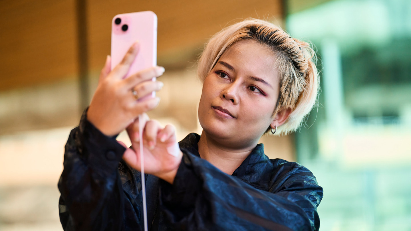 Eine Kundin im Apple Central World in Bangkok macht ein Selfie mit dem iPhone 15 Plus in Rosé.