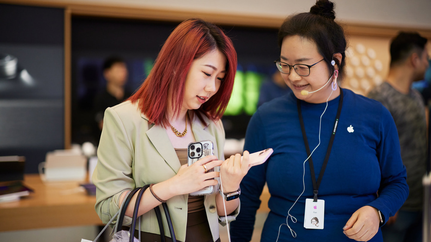 一位顧客拿著粉紅色 iPhone 15，同時與 Apple 南京東路的團隊成員交談。
