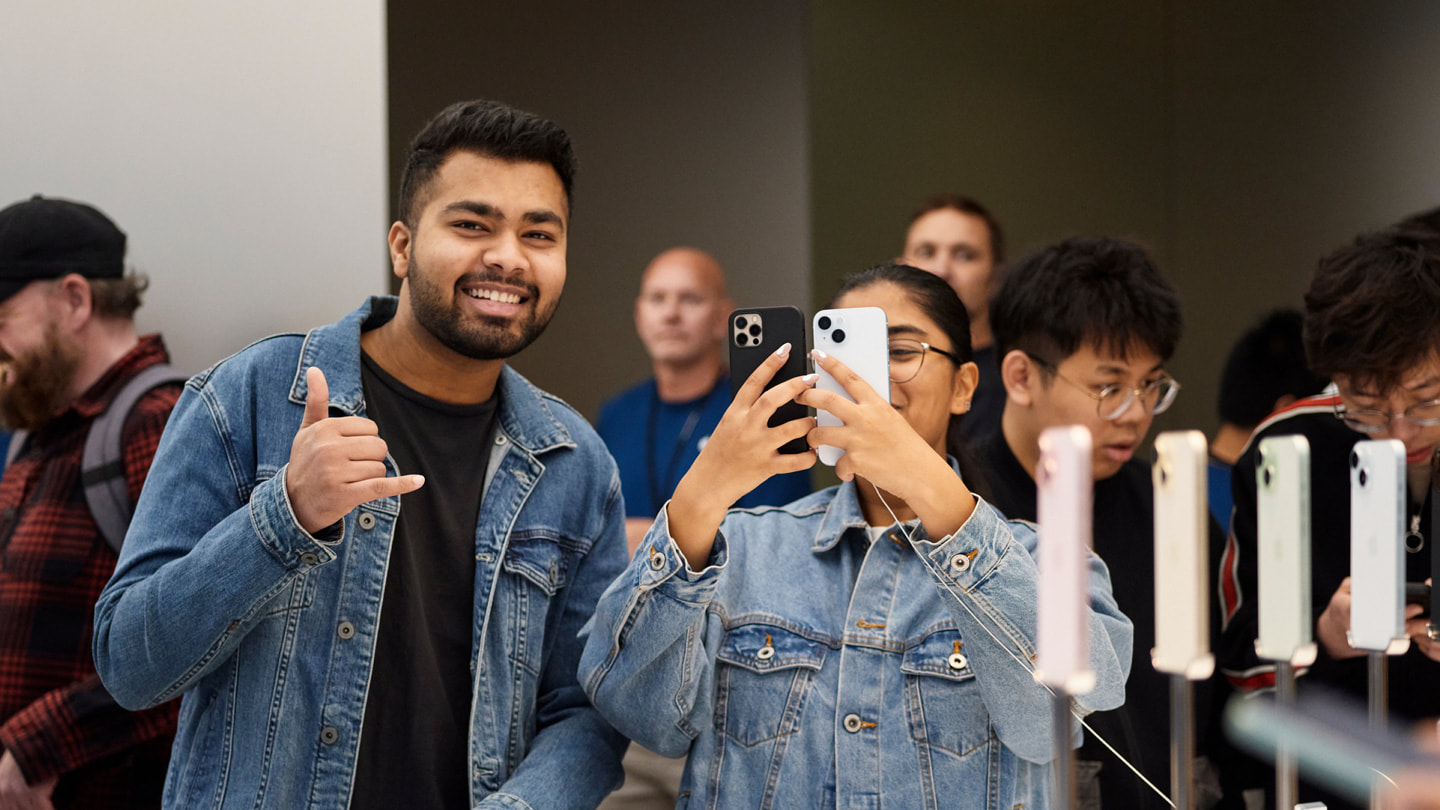 兩名顧客在澳洲的 Apple Sydney 零售店內微笑舉著兩台 iPhone 裝置。