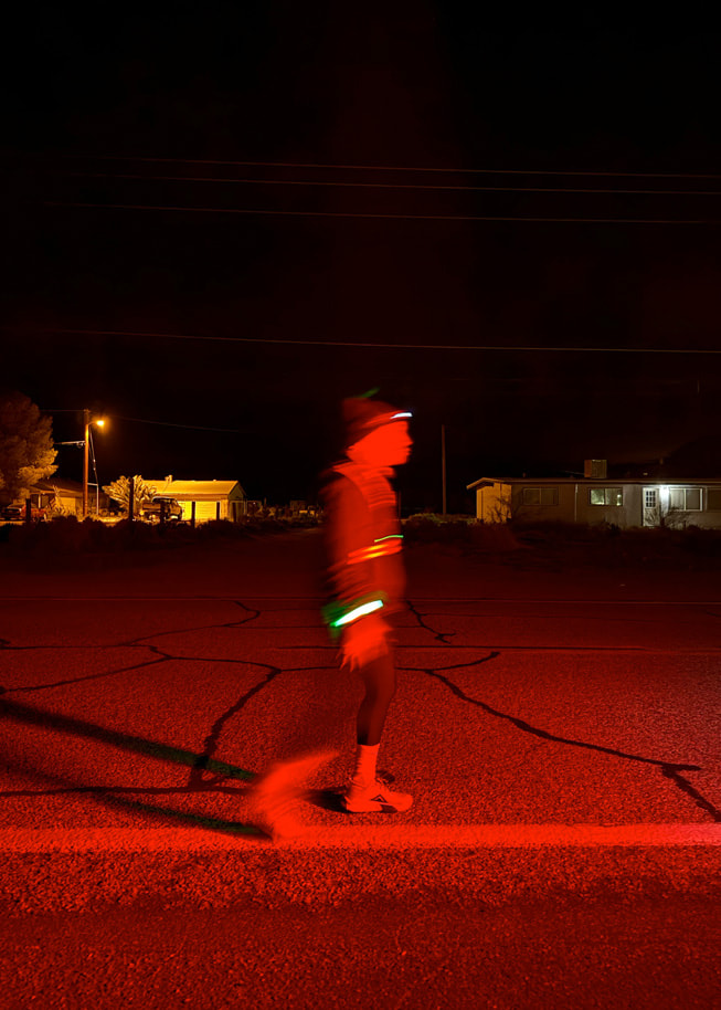 Zdjęcie wykonane nocą na trasie, przedstawiające biegacza z założonymi elementami odblaskowymi.