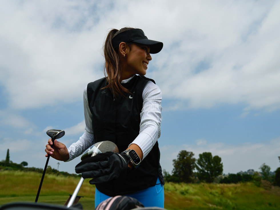 Una golfista con al polso un Apple Watch che tiene in mano due mazze da golf.