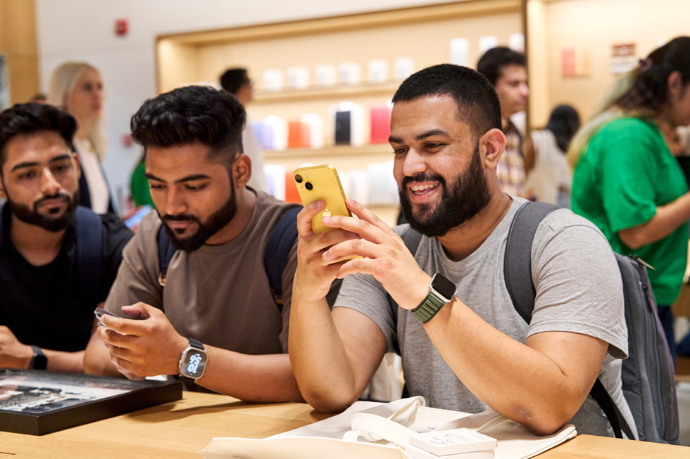 En kunde undersøger iPhone 14 i den nye gule farve siddende ved et bord i Apple Saket.