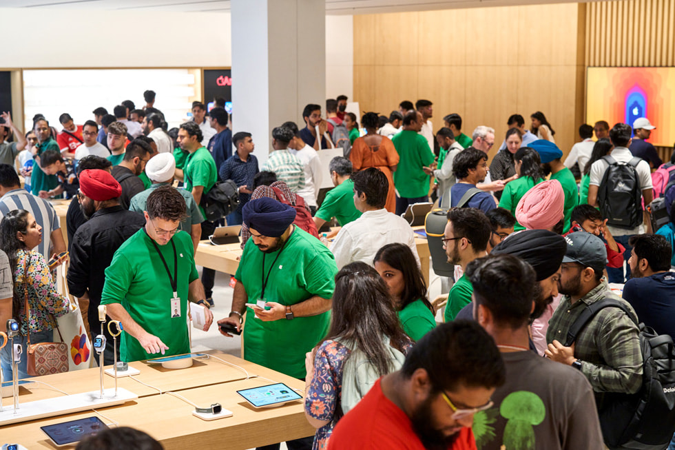 Indenfor i Apple Saket taler kunderne med Apple-medarbejdere og samler sig omkring bordene for at opleve de mange enheder i butikken.
