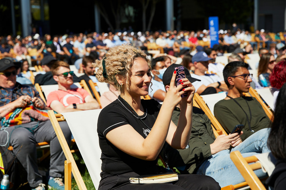 يشاهد الحاضرون العرض التقديمي لمؤتمر WWDC22 خارج Caffè Macs في Apple Park.