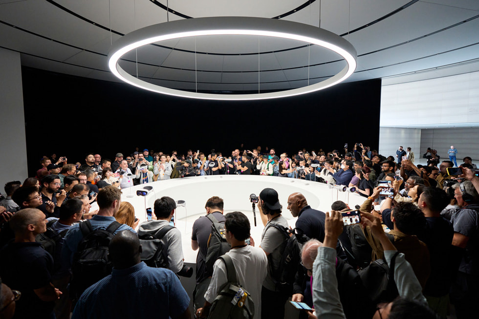 مجموعة من العاملين بالصحافة يقفون حول طاولة عرض تعرض Apple Vision Pro في Apple Park.