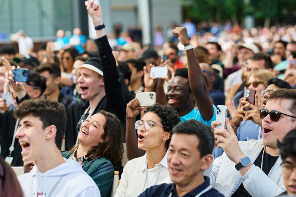 A close-up of developers outdoors at Apple Park cheering and holding up their phones.