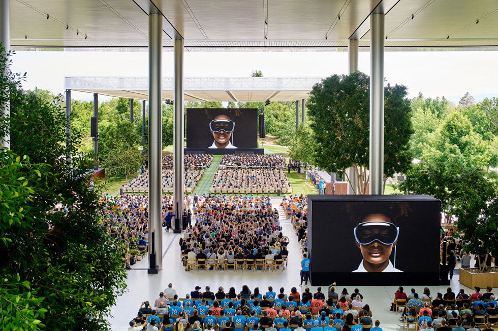 Setki deweloperów oglądają prezentację inaugurującą WWDC23, siedząc na krzesłach ustawionych na terenie Apple Park.