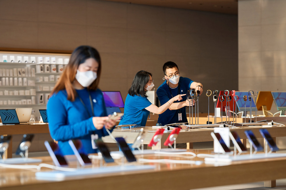Et teammedlem i Apple Sanlitun ser på en iPhone mens to teammedlemmer justerer en AppleWatch-utstilling i bakgrunnen.