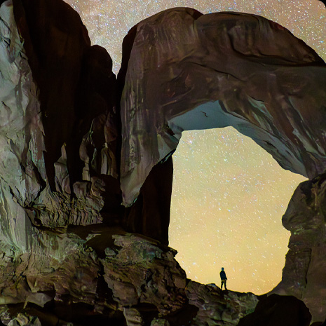 Una fotografia di una persona in un canyon sullo sfondo di un cielo stellato