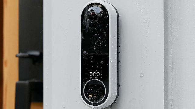 The Arlo video doorbell on a white post in the rain.