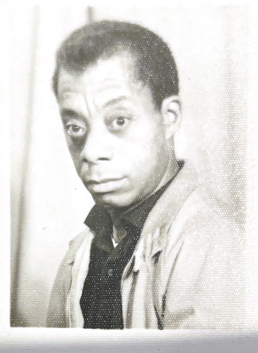 Black and white photo of James Baldwin looking at camera with a serious expression.