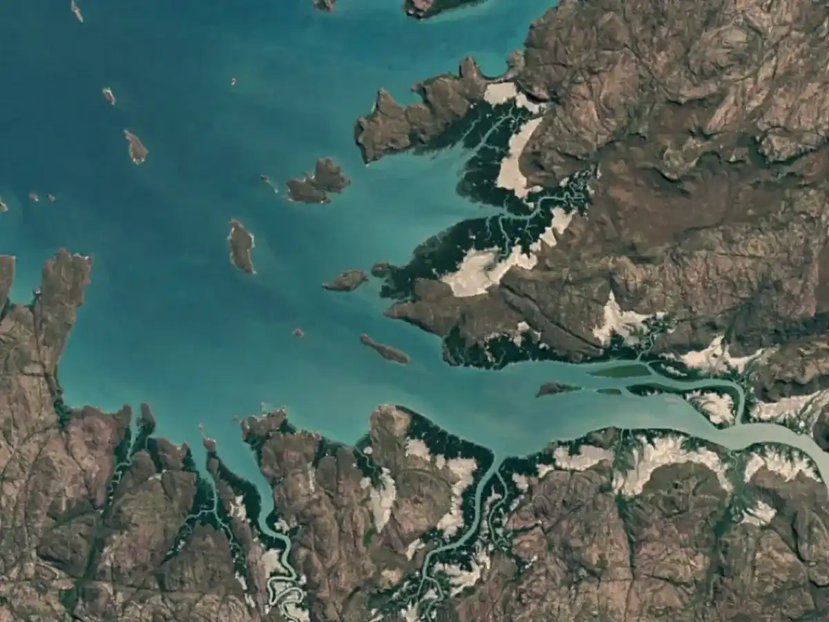 Aerial image showing a tan land mass next to a teal colored body of water