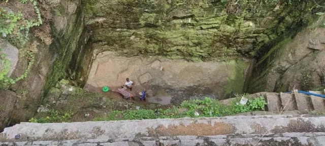 Tres personas limpian el fondo de un pozo de agua.