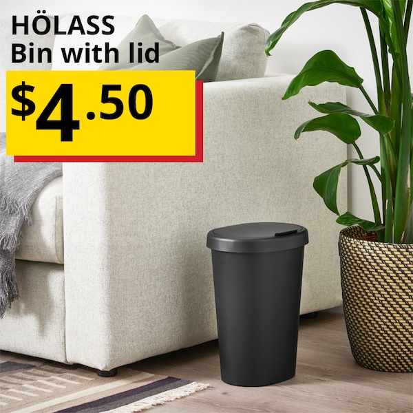 A HÖLASS black bin with lid is placed on the floor next to the a white couch and a large potted plant. A label entitled "HÖLASS Bin with lid" is on the top left of the image. Price $4.50