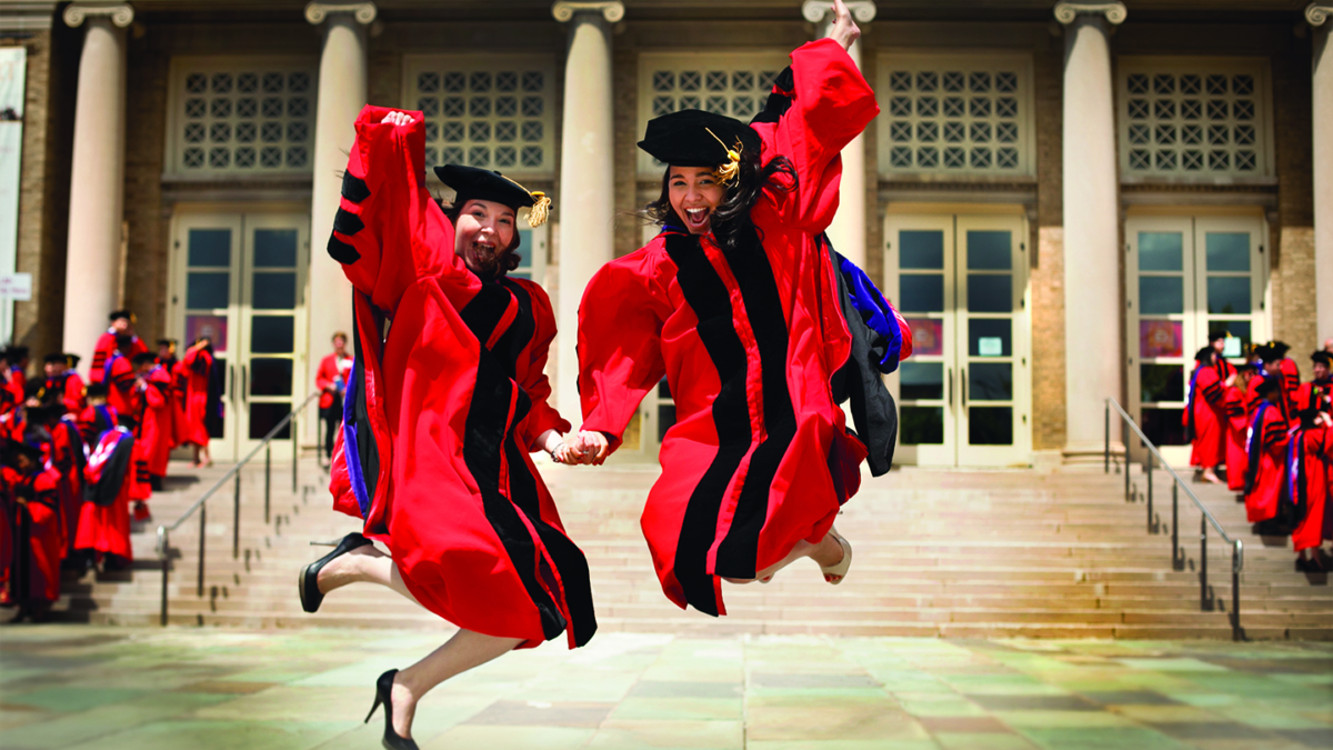 Two students holding hands and jumping in the air, celebrating Convocation