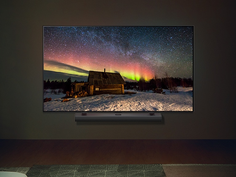 Un LG TV et une barre de son LG dans un salon moderne pendant la nuit. L’écran affiche une image de l’aurore boréale avec une luminosité idéale.