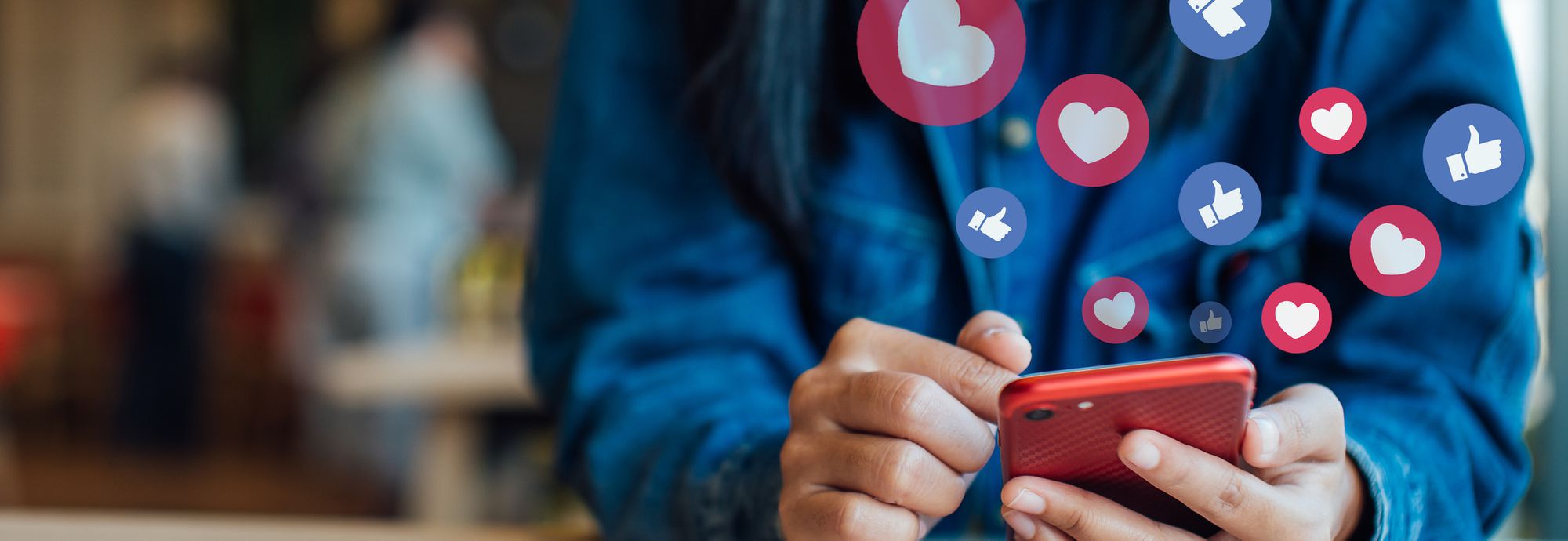 Floating hearts and thumbs-up symbols over a person holding a smartphone.