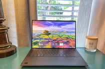 The Dell XPS 14 open on a side table with a lamp and candle and an open window behind it.