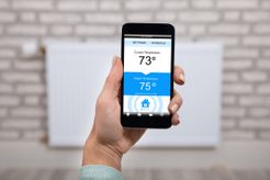 Woman Operating Thermostat Using Smartphone